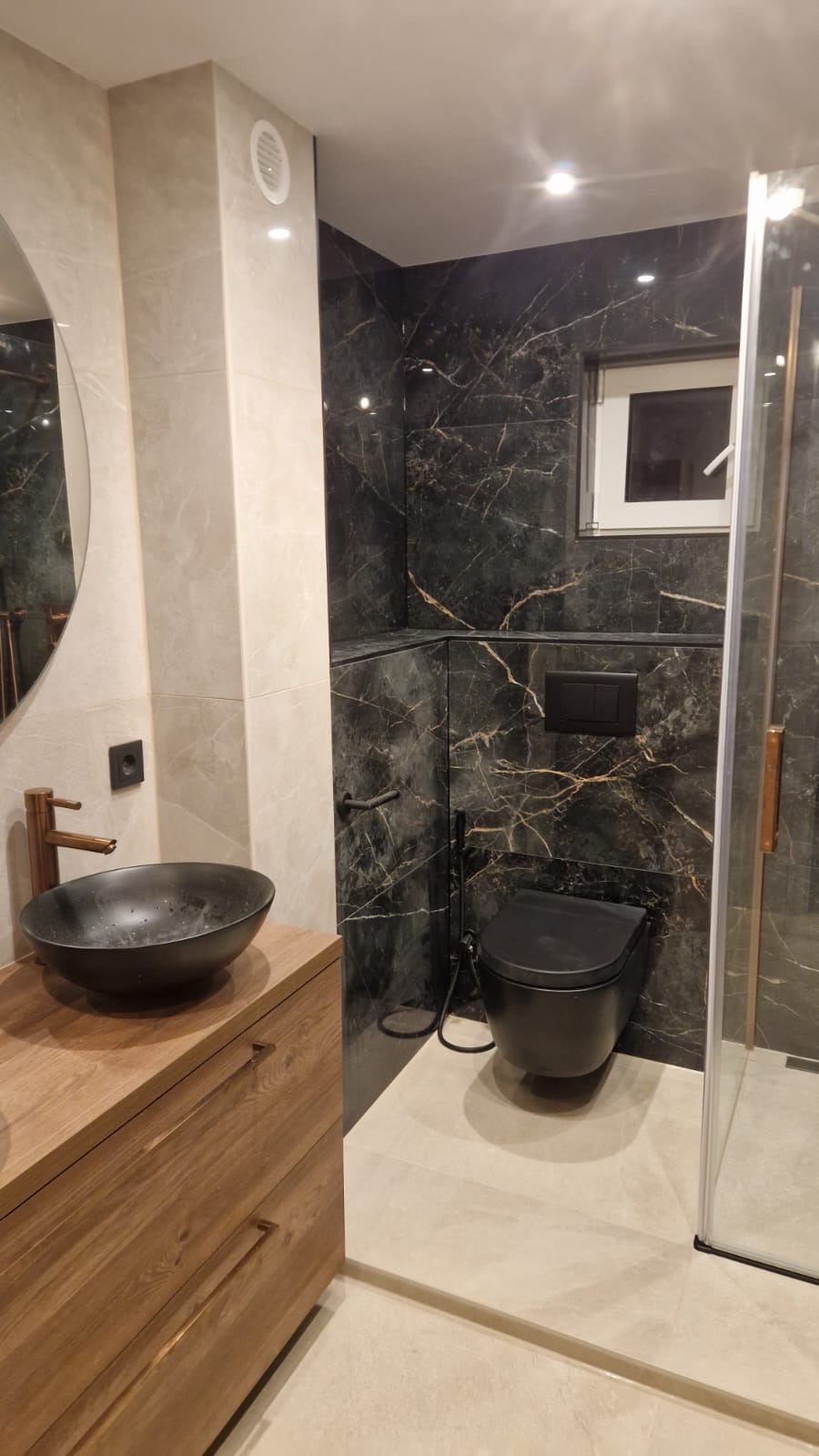 Badkamer met zwart marmerlook tegelwerk, zwart hangtoilet, houten meubel en inloopdouche