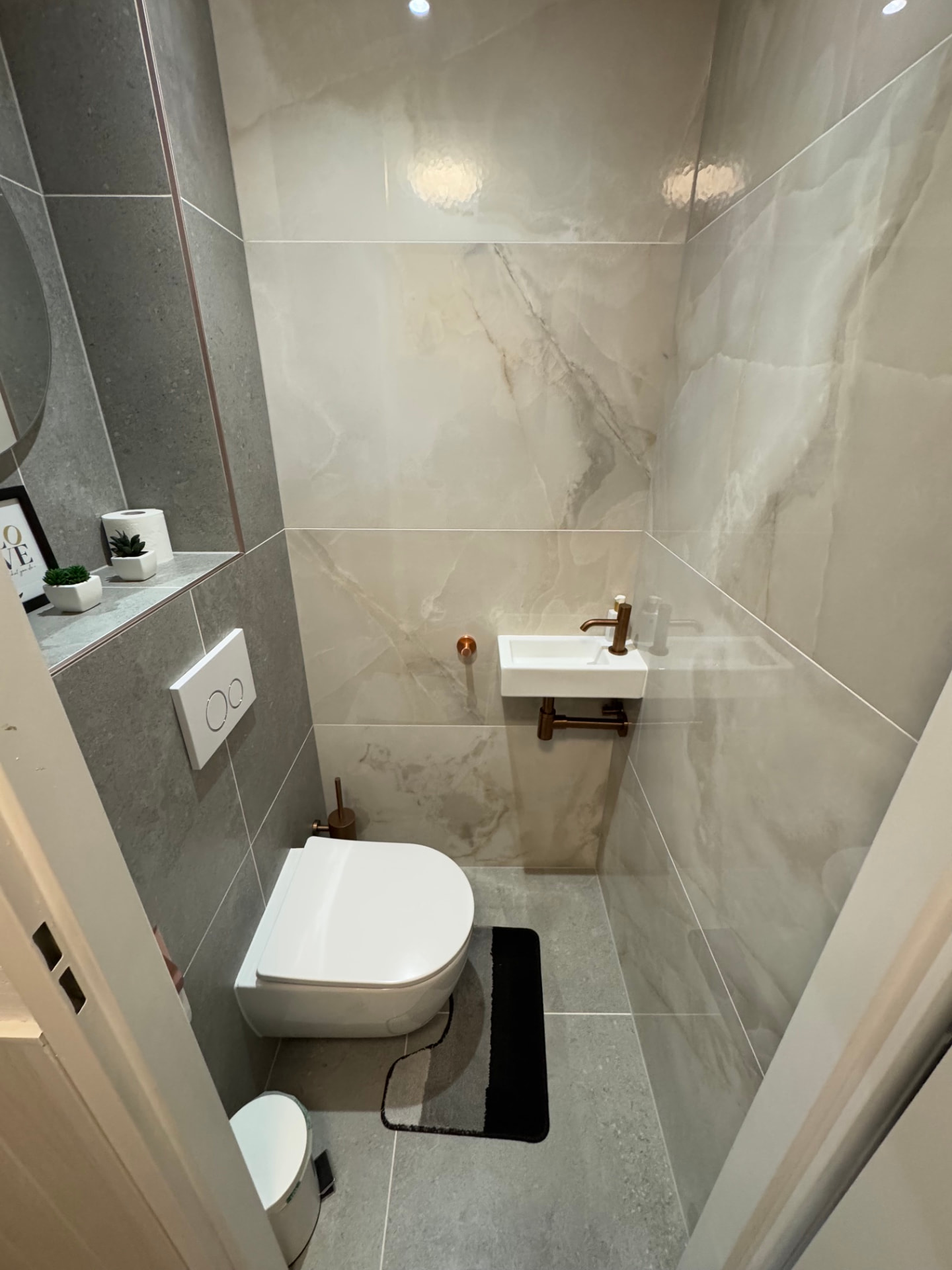 Gerenoveerd toilet met marmerlook tegels en koperen kraan en fontein